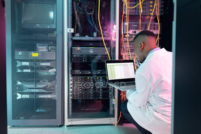Africano americano técnico de computador masculino usando laptop trabalhando na sala de servidores de negócios. armazenamento digital de informações e tecnologia de rede de comunicação. — Fotografia de Stock
