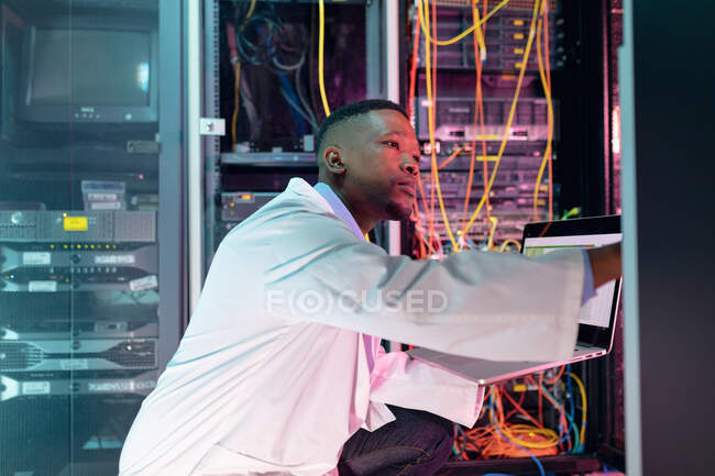 Tecnico informatico afroamericano di sesso maschile che utilizza laptop che lavorano nella sala server aziendale. tecnologia digitale di memorizzazione delle informazioni e rete di comunicazione. — Foto stock