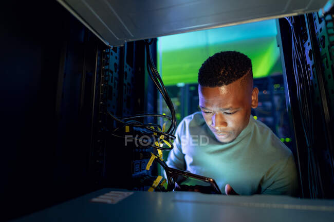 Africano americano técnico de informática do sexo masculino usando tablet e trabalhando na sala de servidores. armazenamento digital de informações e tecnologia de rede de comunicação. — Fotografia de Stock