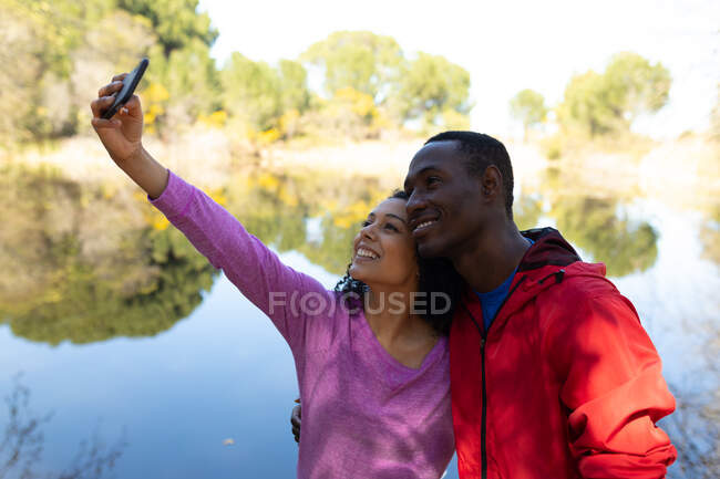 Счастливая пара делает селфи на озере в сельской местности. здоровый, активный уличный образ жизни и досуг. — стоковое фото