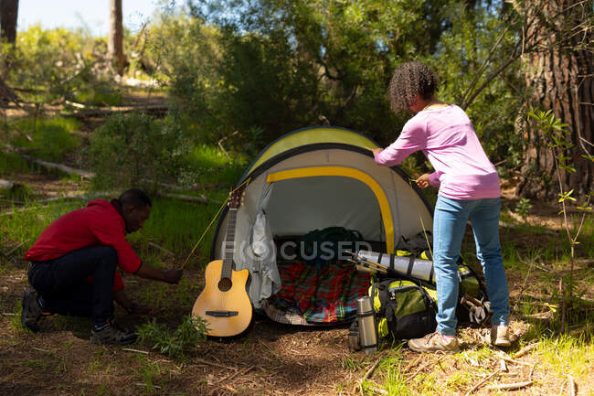 Happy diverse couple putting up the tent in countryside. healthy, active outdoor lifestyle and leisure time. — Stock Photo
