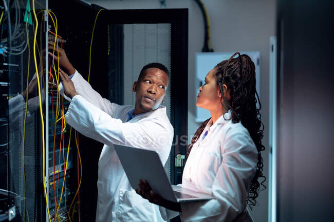 Techniciens informatiques afro-américains utilisant un ordinateur portable travaillant dans la salle des serveurs. stockage de l'information numérique et technologie des réseaux de communication. — Photo de stock