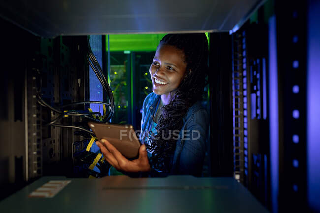 Felice tecnico informatico afroamericano donna utilizzando tablet e lavorando in sala server. tecnologia digitale di memorizzazione delle informazioni e rete di comunicazione. — Foto stock