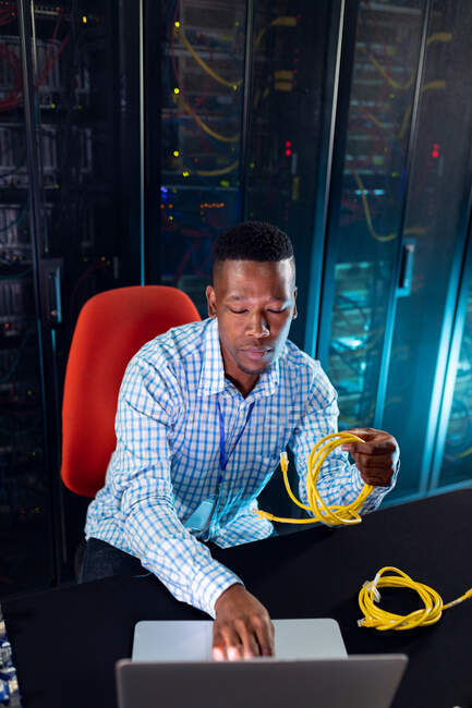 Homme technicien informatique afro-américain utilisant un ordinateur portable travaillant dans la salle des serveurs. stockage de l'information numérique et technologie des réseaux de communication. — Photo de stock