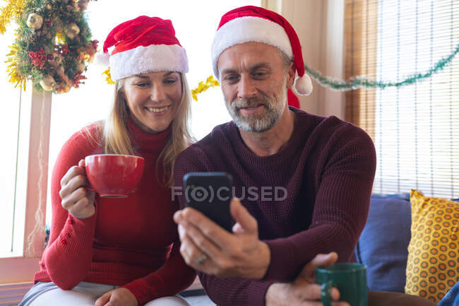 Glückliches kaukasisches Ehepaar telefoniert zu Weihnachten per Smartphone. Weihnachten, Fest und Kommunikationstechnologie. — Stockfoto