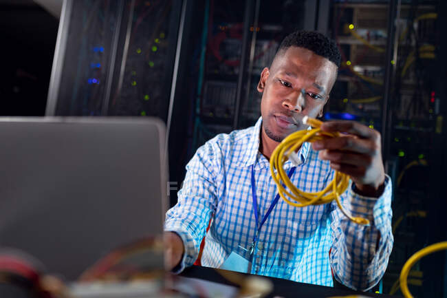 Sorrindo afro-americano homem técnico de informática usando laptop trabalhando na sala de servidores de negócios. armazenamento digital de informações e tecnologia de rede de comunicação. — Fotografia de Stock