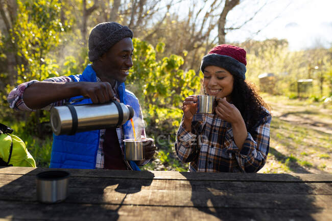 Diverse couple drinking coffee and taking break from hiking in countryside. healthy, active outdoor lifestyle and leisure time. — Stock Photo