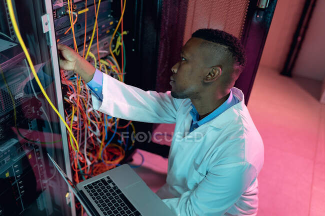 Tecnico informatico afroamericano di sesso maschile che utilizza laptop che lavorano nella sala server aziendale. tecnologia digitale di memorizzazione delle informazioni e rete di comunicazione. — Foto stock