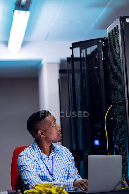 Lächelnder afrikanischer Computertechniker mit Laptop, der im Serverraum für Unternehmen arbeitet. digitale Informationsspeicherung und Kommunikations-Netzwerktechnologie. — Stockfoto