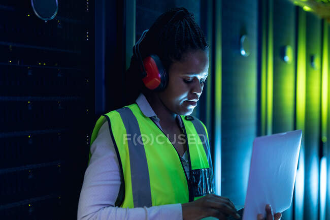 Tecnico informatico afroamericano che indossa cuffie usando laptop che lavorano nella sala server. tecnologia digitale di memorizzazione delle informazioni e rete di comunicazione. — Foto stock