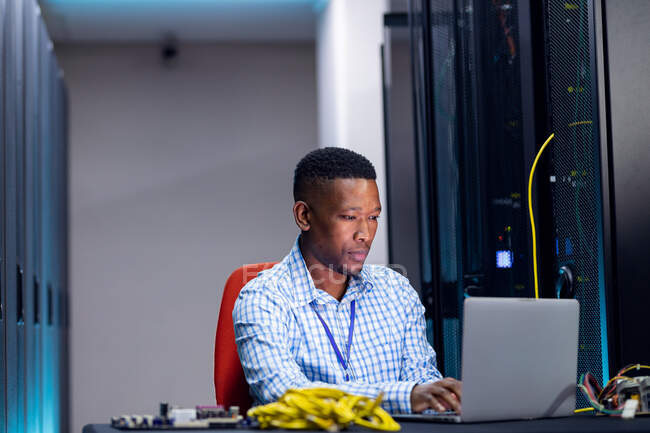 Smiling african american male computer technician using laptop working in business server room. digital information storage and communication network technology. — Stock Photo