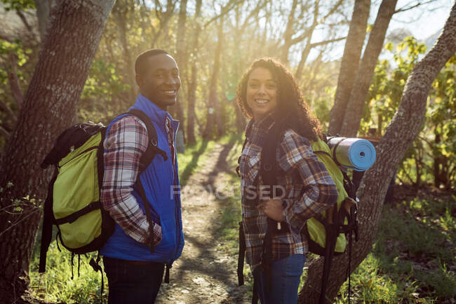 Счастливая разносторонняя пара с рюкзаками, прогуливающаяся по сельской местности. здоровый, активный уличный образ жизни и досуг. — стоковое фото
