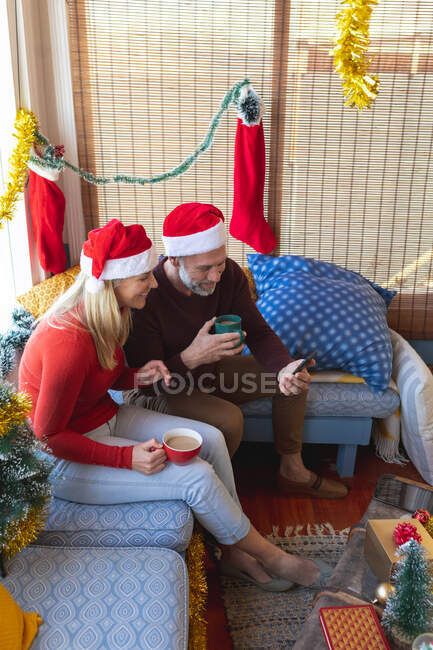 Heureux couple d'âge mûr caucasien boire du café, faire un appel vidéo à Noël. Noël, fête et technologie de la communication. — Photo de stock
