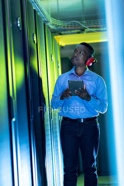 Afrikanisch-amerikanischer Computertechniker mit Kopfhörern und Tablet im Serverraum. digitale Informationsspeicherung und Kommunikations-Netzwerktechnologie. — Stockfoto