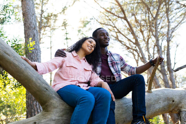 Couple diversifié assis sur une branche dans la forêt. mode de vie sain et actif en plein air et temps libre. — Photo de stock