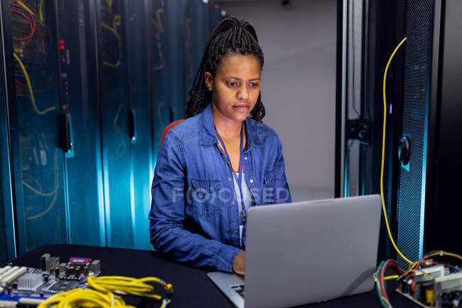 African american female computer technician using laptop working in server room. digital information storage and communication network technology. — Stock Photo