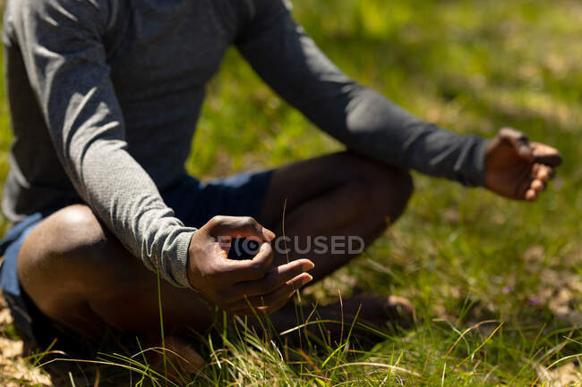 Relaxante homem afro-americano sentado com pernas cruzadas e meditando no campo. saudável, estilo de vida ao ar livre ativo e tempo de lazer. — Fotografia de Stock