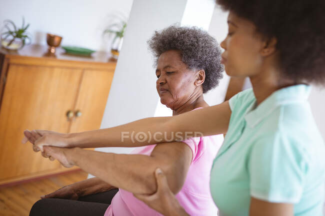 Fisioterapeuta afro-americana a tratar braços de uma paciente idosa na clínica. cuidados de saúde seniores e tratamento de fisioterapia médica. — Fotografia de Stock