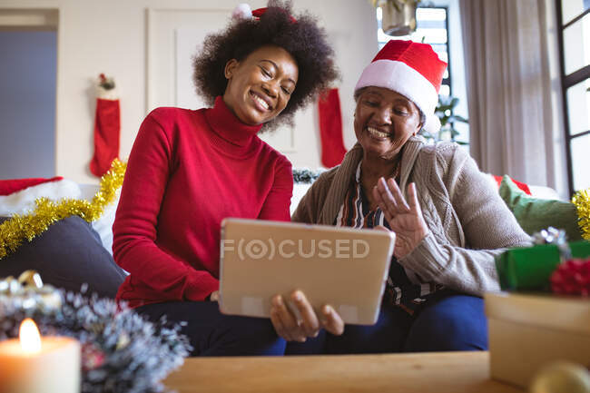 Heureuse femme âgée afro-américaine et fille adulte en chapeaux Santa faire appel vidéo de Noël. Noël, fête et technologie de la communication. — Photo de stock