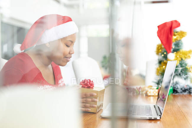 Feliz afroamericana más mujer de tamaño en sombrero de santa haciendo videollamada de Navidad en el ordenador portátil. navidad, festividad y tecnología de la comunicación. - foto de stock