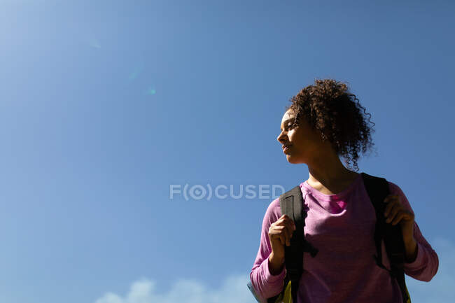 Mulher biracial relaxada com mochilas no céu azul. saudável, estilo de vida ao ar livre ativo e tempo de lazer. — Fotografia de Stock