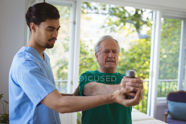 Biracial male physiotherapist treating arms of senior male patient at clinic. senior healthcare and medical physiotherapy treatment. — Stock Photo