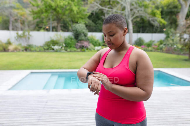 Afro americano más mujer de tamaño en ropa deportiva mirando smartwatch en el jardín. fitness y estilo de vida saludable y activo. - foto de stock
