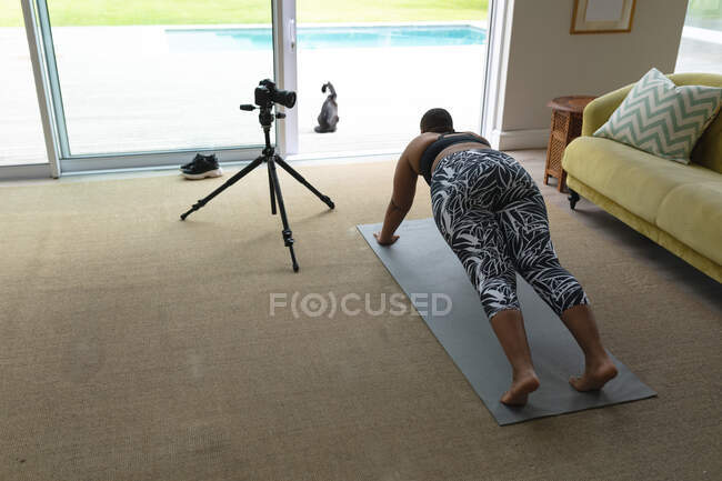 Feliz afroamericana mujer de talla grande grabando práctica de yoga en casa. fitness y estilo de vida saludable y activo. - foto de stock