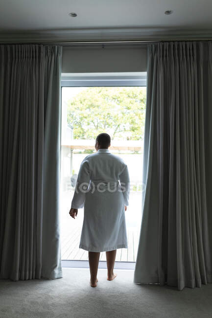 Vista posteriore della donna afro-americana plus size in piedi alla finestra. stile di vita, tempo libero e trascorrere del tempo a casa. — Foto stock