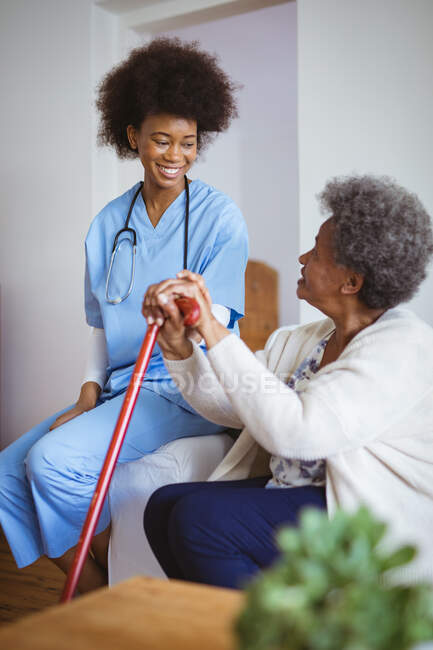 Médecin afro-américain souriant tenant la main d'une patiente âgée à la maison. soins de santé et mode de vie pendant la pandémie de covide 19. — Photo de stock