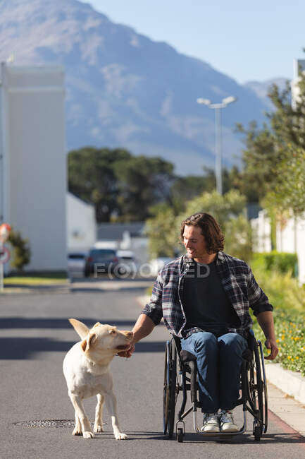 Uomo disabile caucasico con cane seduto sulla sedia a rotelle sulla strada. concetto di disabilità e handicap — Foto stock