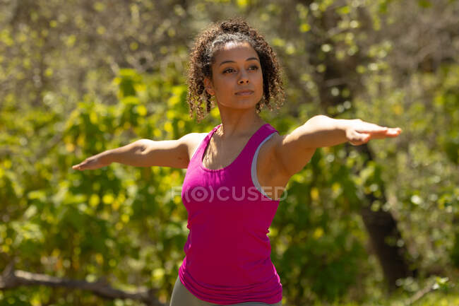 Relaxing biracial woman practicing yoga, standing and practicing yoga in countryside. healthy, active outdoor lifestyle and leisure time. — Stock Photo
