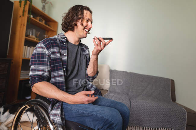 Kaukasischer behinderter Mann, der im Rollstuhl sitzt und zu Hause mit dem Smartphone spricht. Behinderten- und Behindertenkonzept — Stockfoto