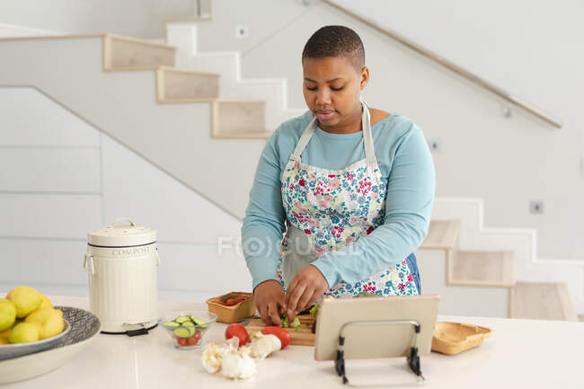 Африканський американець плюс жінка в розмірах ріже овочі, використовуючи планшет на кухні. спосіб життя, приготування їжі та перебування вдома. — стокове фото