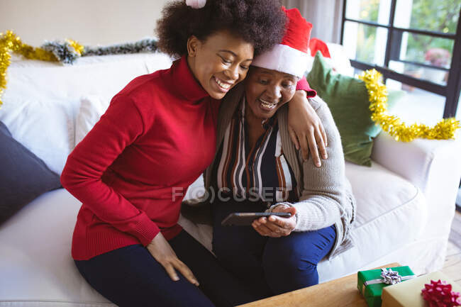 Glückliche afrikanisch-amerikanische Seniorin und erwachsene Tochter in Weihnachtsmützen, die Weihnachtsvideo anrufen. Weihnachten, Fest und Kommunikationstechnologie. — Stockfoto