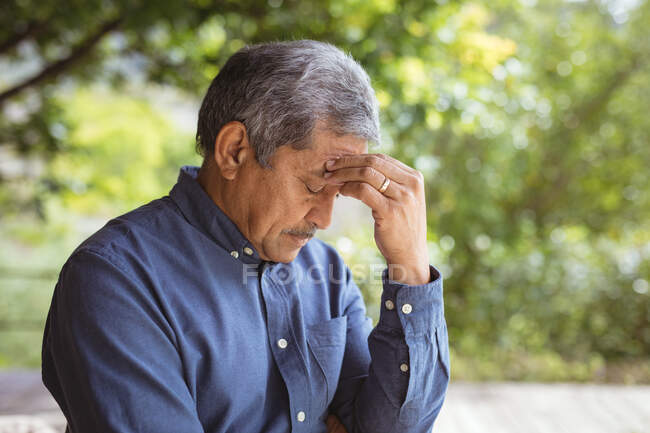 Senior biracial man touching his forehead and thinking in garden. spending time at home alone. — Stock Photo