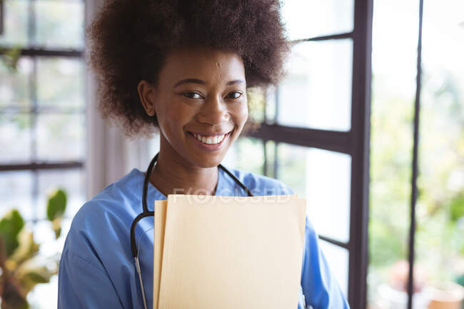 Porträt einer lächelnden afrikanisch-amerikanischen Ärztin mit Dokumenten. Gesundheitswesen und Lebensstil während der Covid 19 Pandemie. — Stockfoto