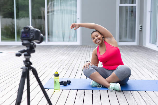Heureuse femme afro-américaine plus la taille dans les vêtements de sport pratiquant le yoga, ce qui rend vlog. forme physique et mode de vie sain et actif. — Photo de stock