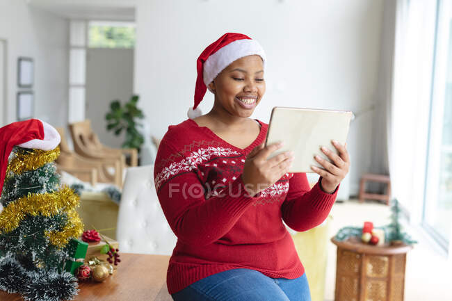 Heureuse femme africaine américaine plus la taille dans le chapeau de Père Noël faire appel vidéo de Noël sur tablette. Noël, fête et technologie de la communication. — Photo de stock