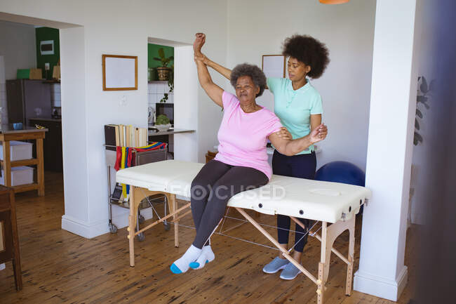 Fisioterapeuta afro-americana a tratar costas de uma paciente idosa na clínica. cuidados de saúde seniores e tratamento de fisioterapia médica. — Fotografia de Stock