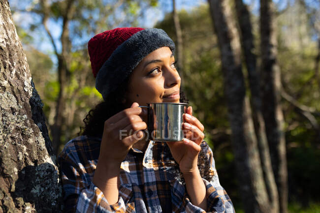 Mulher biracial feliz bebendo café e fazendo uma pausa de caminhadas no campo. saudável, estilo de vida ao ar livre ativo e tempo de lazer. — Fotografia de Stock