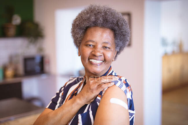 Ritratto di donna afroamericana anziana sorridente che mostra bende sul braccio dopo vaccinazioni virili. assistenza sanitaria e stile di vita durante la pandemia della congrega 19. — Foto stock