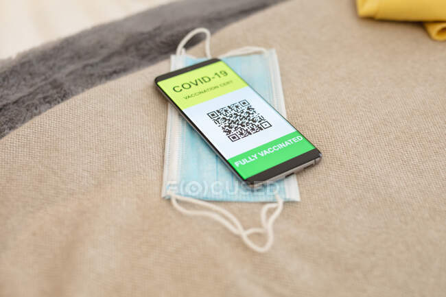 Smartphone with covid passport and face mask lying on bed. travel preparation during covid 19 pandemic. — Stock Photo