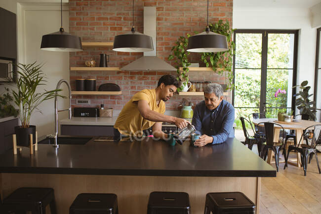 Hijo adulto birracial y padre mayor bebiendo café en la cocina. tiempo en familia en casa juntos. - foto de stock