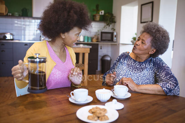 Eine afroamerikanische Seniorin mit erwachsener Tochter, die in der Küche redet und Kaffee trinkt. Familienzeit zu Hause zusammen. — Stockfoto