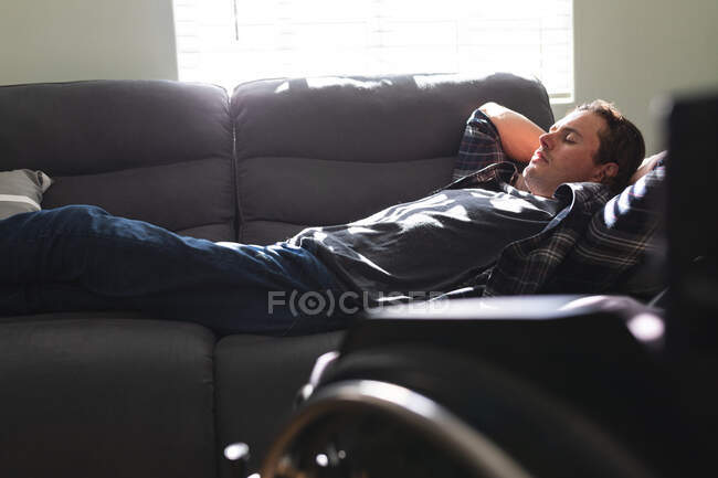 Белый инвалид дремлет дома на диване. Концепция инвалидности и инвалидности — стоковое фото