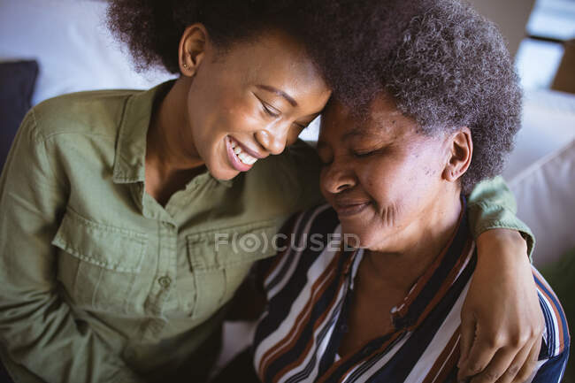 Улыбающаяся африканская пожилая американка со взрослой дочерью, обнимающаяся с закрытыми глазами. семейное время дома вместе. — стоковое фото