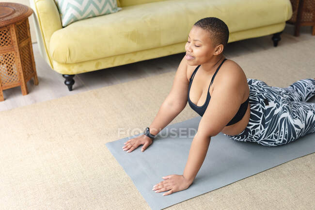Счастливый африканский американец плюс размер женщина практикует йогу на коврике дома. фитнес и здоровый, активный образ жизни. — стоковое фото
