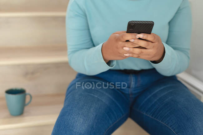 Midsection of plus size woman making call and drinking coffee on stairs. lifestyle, leisure, spending time at home with technology. — Stock Photo