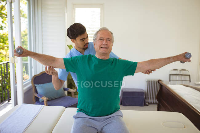 Fisioterapeuta Biracial masculino tratando de nuevo a un paciente masculino mayor en la clínica. atención médica de alto nivel y tratamiento de fisioterapia médica. - foto de stock
